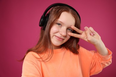 Photo of Beautiful freckled teenage girl with headphones taking selfie on pink background