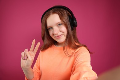 Photo of Beautiful freckled teenage girl with headphones taking selfie on pink background