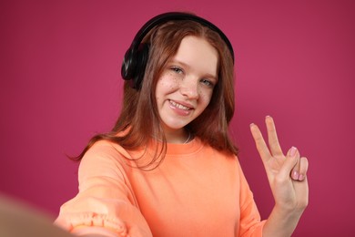 Photo of Beautiful freckled teenage girl with headphones taking selfie on pink background