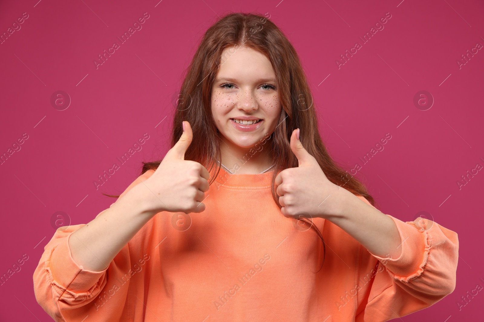 Photo of Beautiful teenage girl with freckles showing thumbs up on pink background