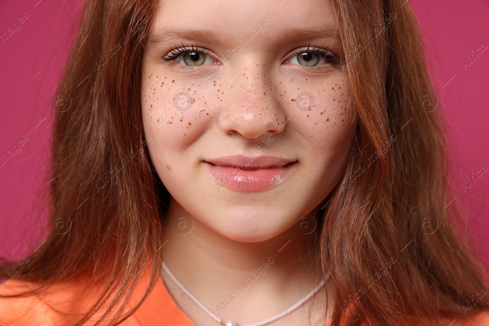 Photo of Beautiful teenage girl with freckles on pink background, closeup