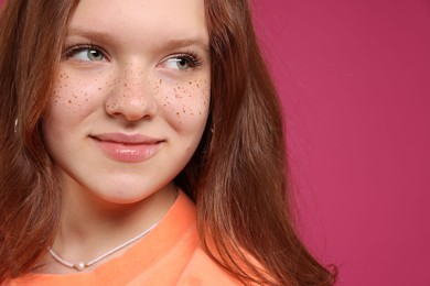 Photo of Beautiful teenage girl with freckles on pink background, closeup. Space for text