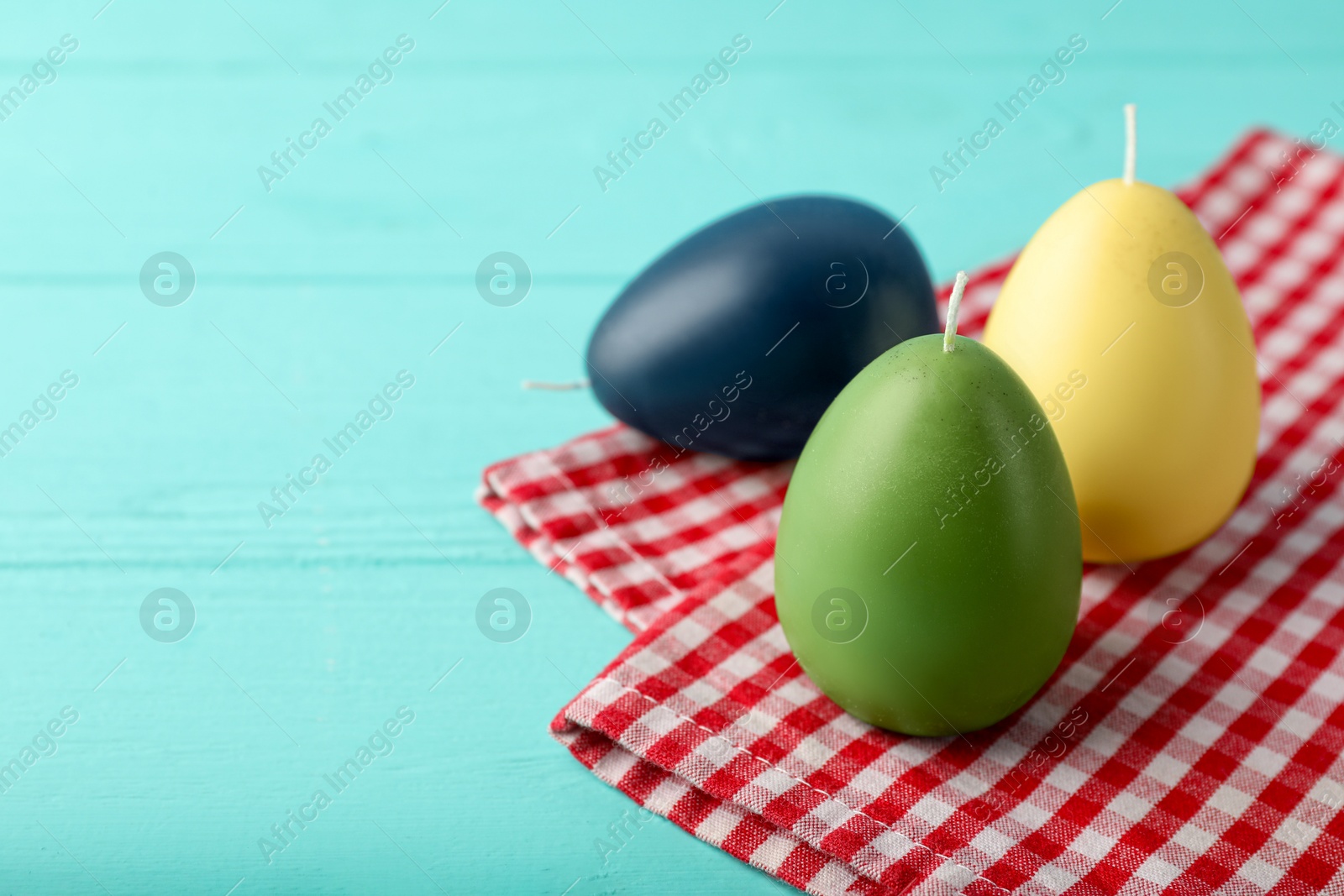 Photo of Colorful egg-shaped candles on turquoise wooden table, closeup and space for text. Easter decor