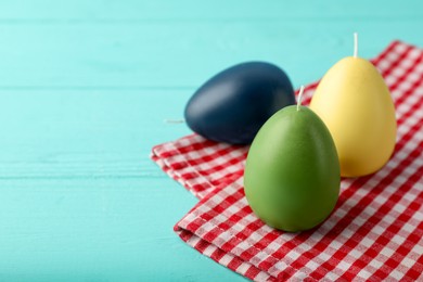 Photo of Colorful egg-shaped candles on turquoise wooden table, closeup and space for text. Easter decor