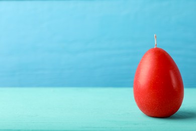 Photo of Red egg-shaped candle on turquoise wooden table against light blue background, space for text. Easter decor