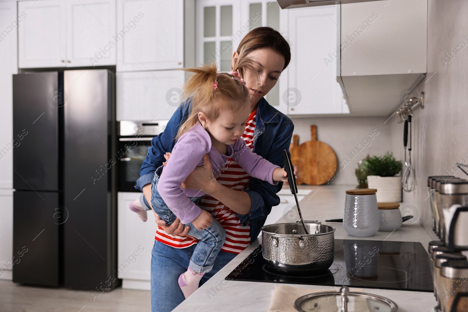 Photo of Busy housewife cooking with her little daughter in kitchen