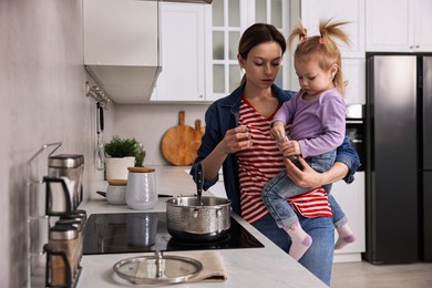 Photo of Busy housewife cooking with her little daughter in kitchen