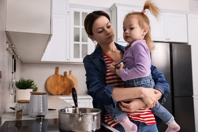 Photo of Busy housewife cooking with her little daughter in kitchen