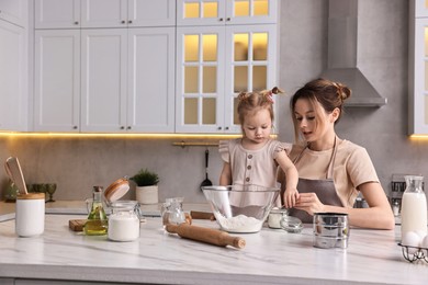 Photo of Housewife cooking with her little daughter at marble table in kitchen