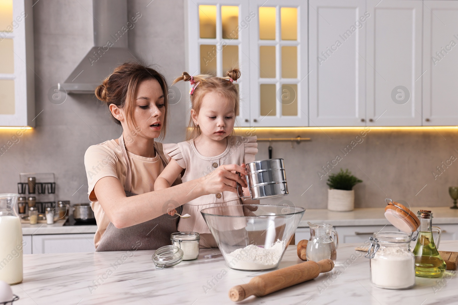 Photo of Housewife cooking with her little daughter at marble table in kitchen