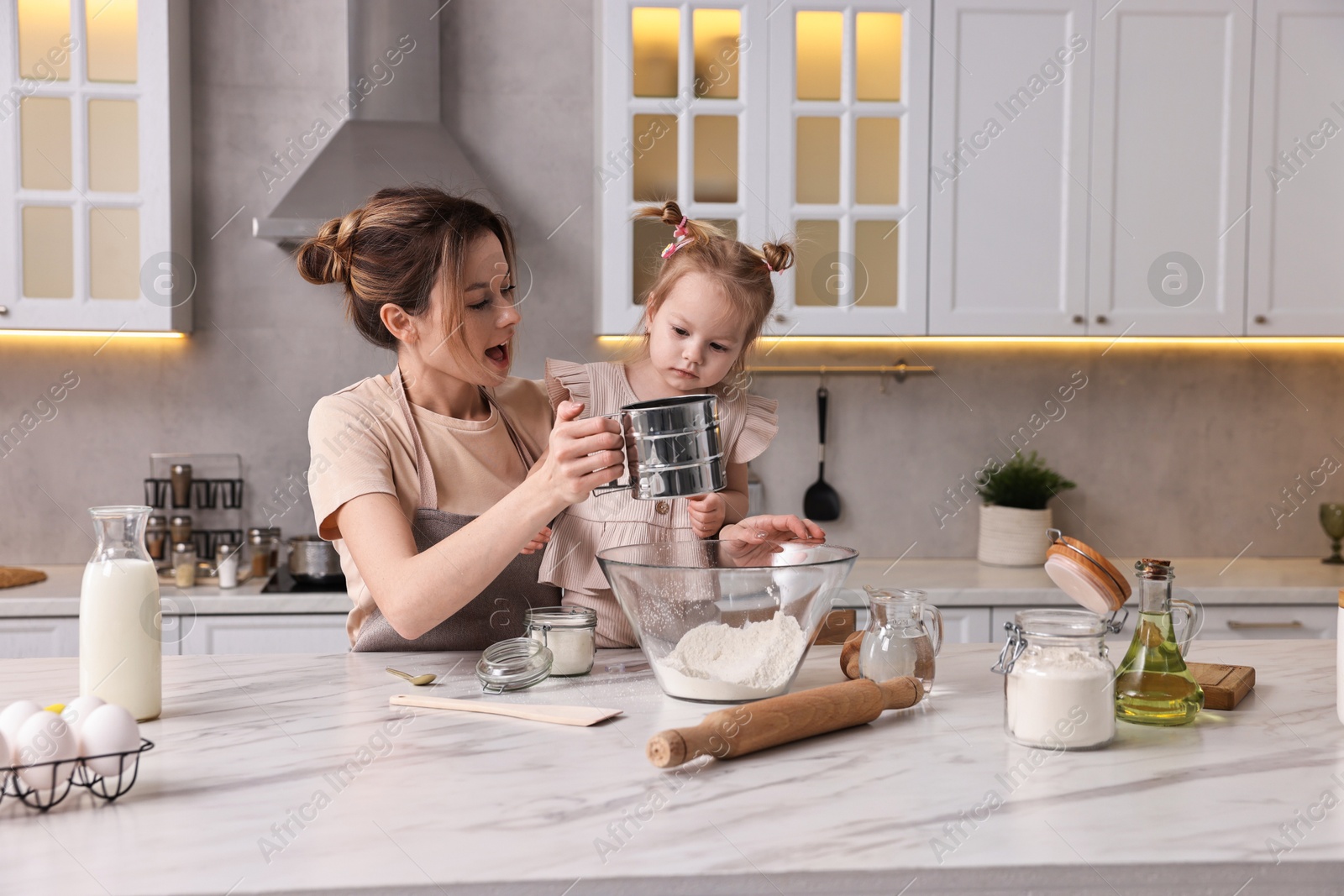 Photo of Housewife cooking with her little daughter at marble table in kitchen