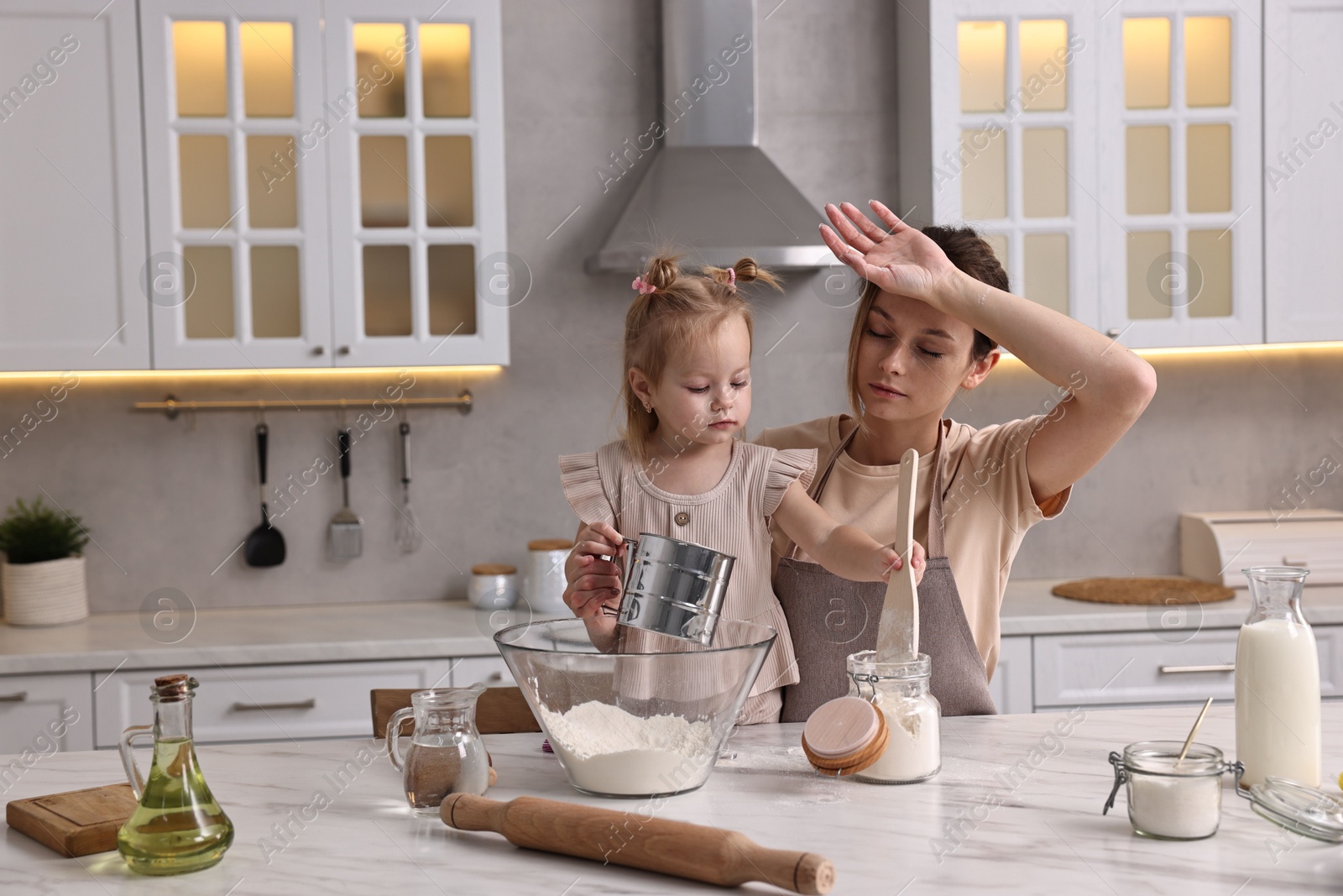 Photo of Tired housewife cooking with her little daughter at marble table in kitchen