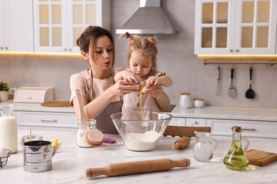 Housewife cooking with her little daughter at marble table in kitchen