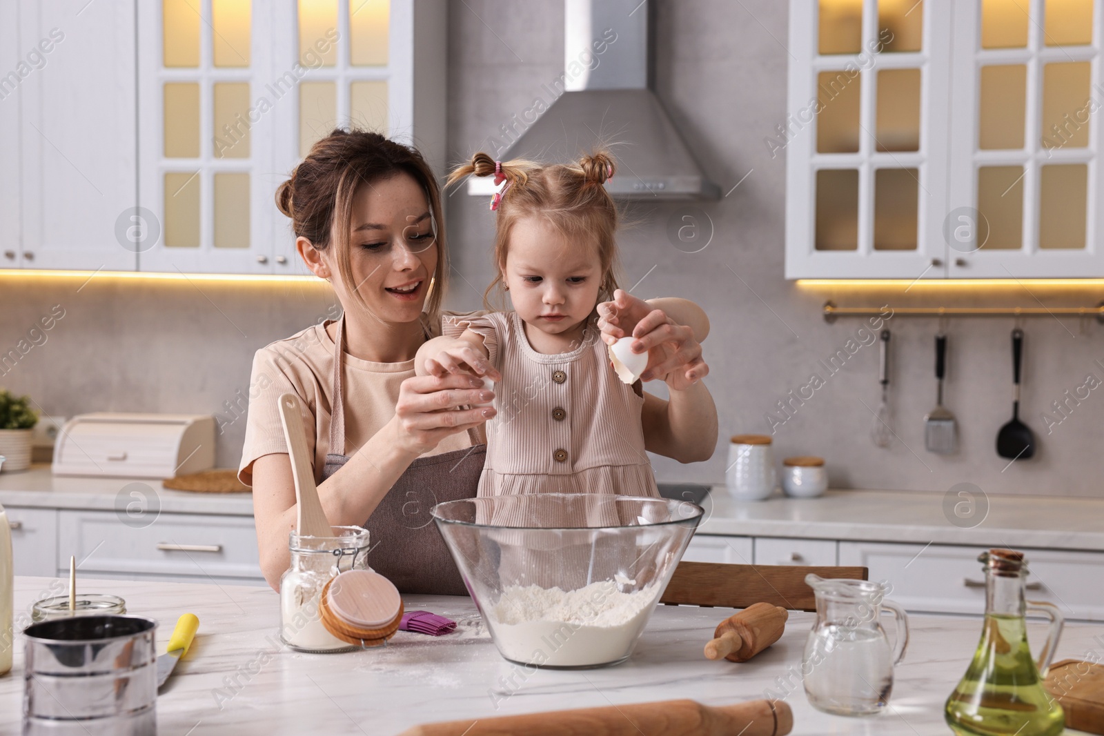 Photo of Smiling housewife cooking with her little daughter at marble table in kitchen