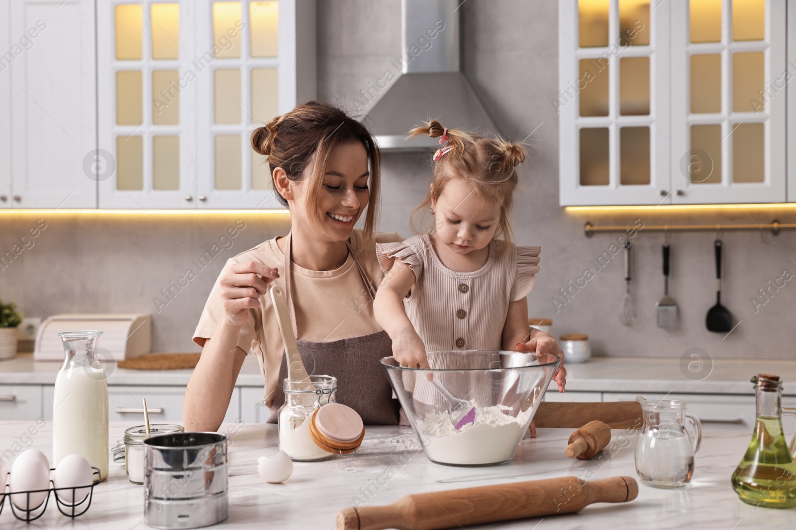 Photo of Smiling housewife cooking with her little daughter at marble table in kitchen