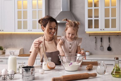 Smiling housewife cooking with her little daughter at marble table in kitchen