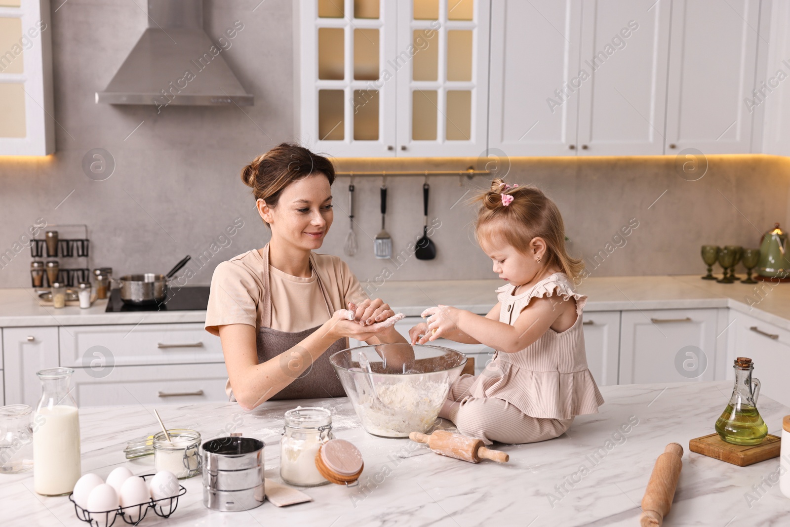 Photo of Housewife cooking with her little daughter at marble table in kitchen