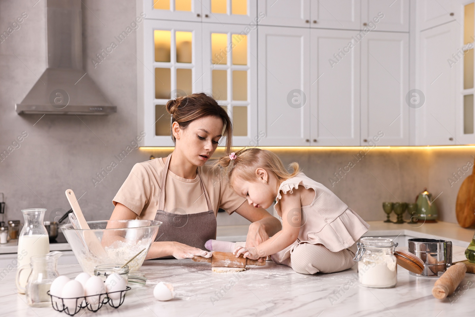 Photo of Housewife cooking with her little daughter at marble table in kitchen