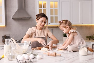 Photo of Smiling housewife cooking with her little daughter at marble table in kitchen