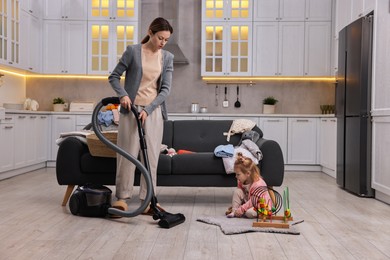 Housewife cleaning floor with vacuum cleaner while her little daughter playing at home