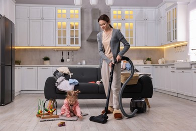 Housewife cleaning floor with vacuum cleaner while her little daughter playing at home