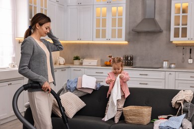 Photo of Housewife cleaning with vacuum cleaner near sofa and her little daughter at home