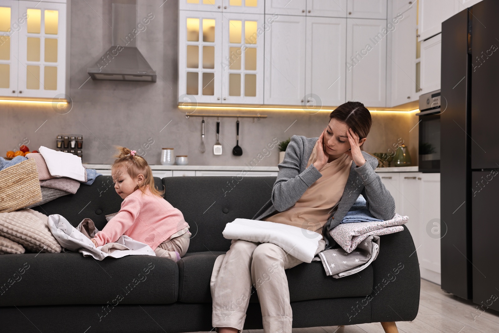 Photo of Housewife with her little daughter folding laundry on sofa at home