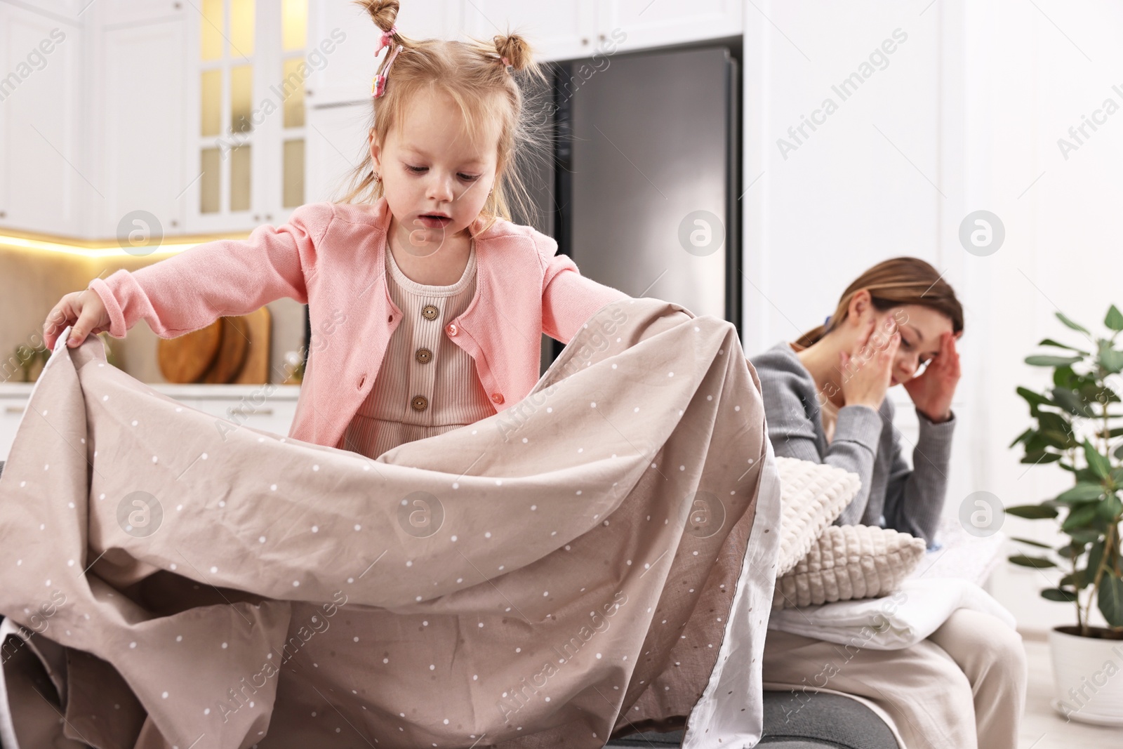 Photo of Tired housewife with her little daughter among messy laundry on sofa at home