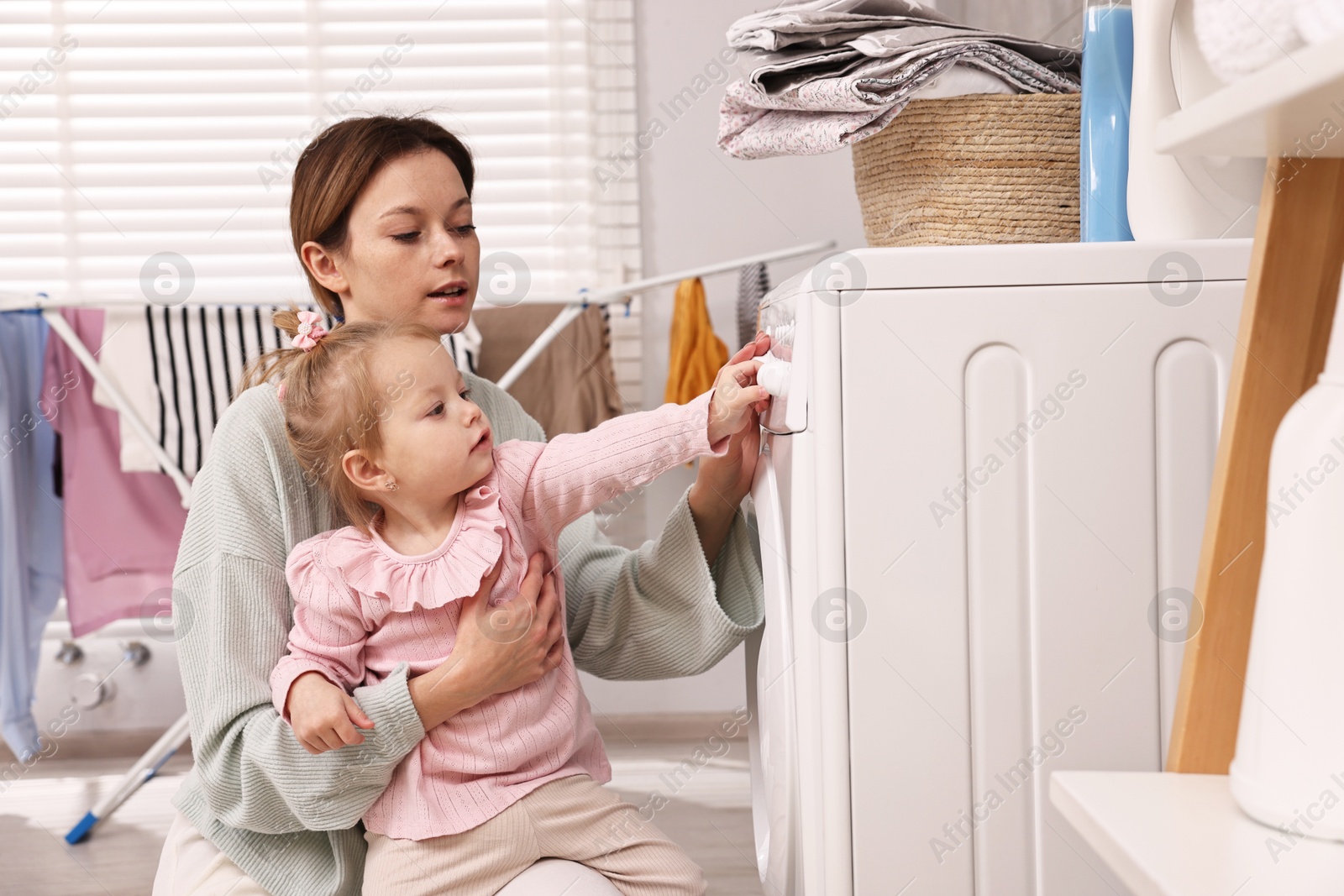 Photo of Housewife with her little daughter doing laundry at home