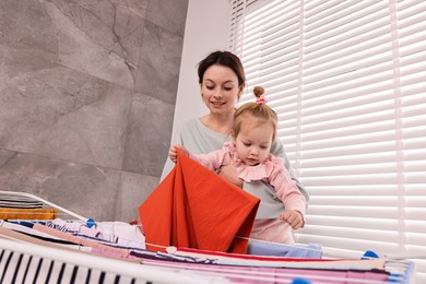 Smiling housewife with her daughter hanging clothes on drying rack at home, low angle view