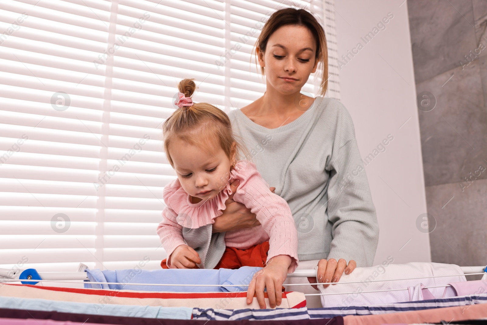 Photo of Housewife with her daughter hanging clothes on drying rack at home