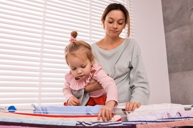 Photo of Housewife with her daughter hanging clothes on drying rack at home