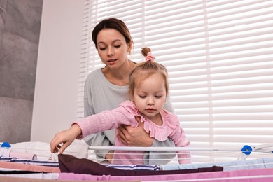 Photo of Housewife with her daughter hanging clothes on drying rack at home