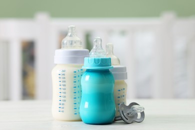 Photo of Feeding bottles with milk and pacifier on white wooden table indoors