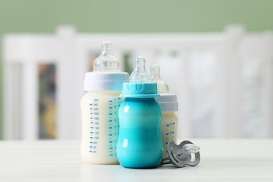 Photo of Feeding bottles with milk and pacifier on white wooden table indoors