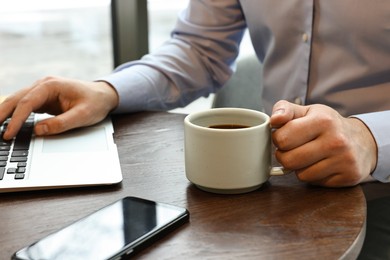 Photo of Businessman having coffee break at wooden table in cafe, closeup