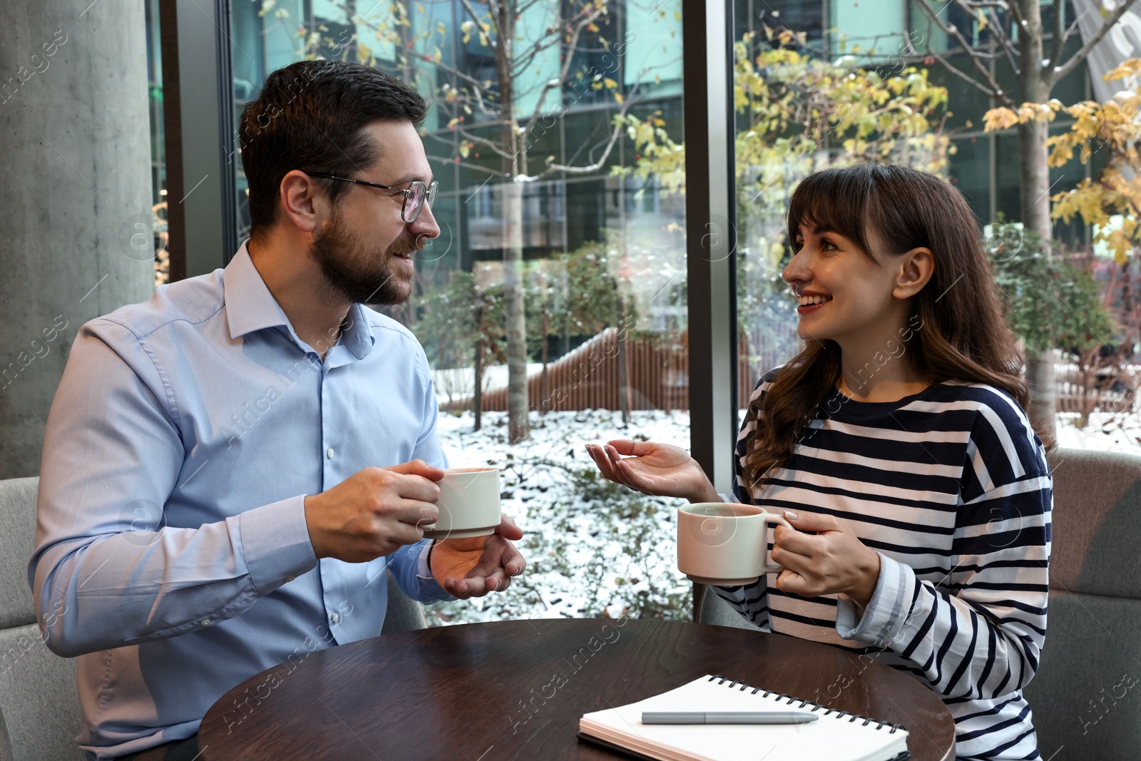 Photo of Happy colleagues talking during coffee break at wooden table in cafe