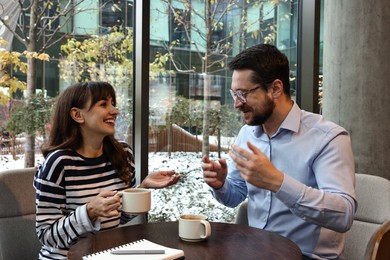 Photo of Happy colleagues talking during coffee break at wooden table in cafe