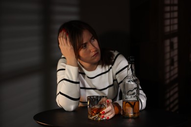 Photo of Alcohol addiction. Woman with glass of whiskey and bottle at table indoors