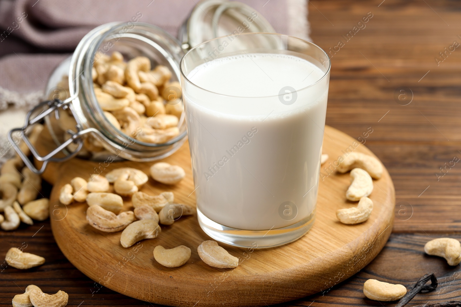 Photo of Fresh cashew milk in glass and nuts on wooden table, closeup