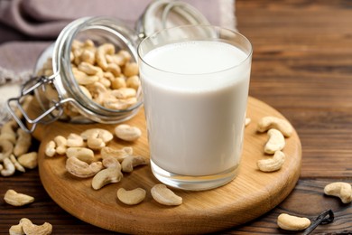 Photo of Fresh cashew milk in glass and nuts on wooden table, closeup