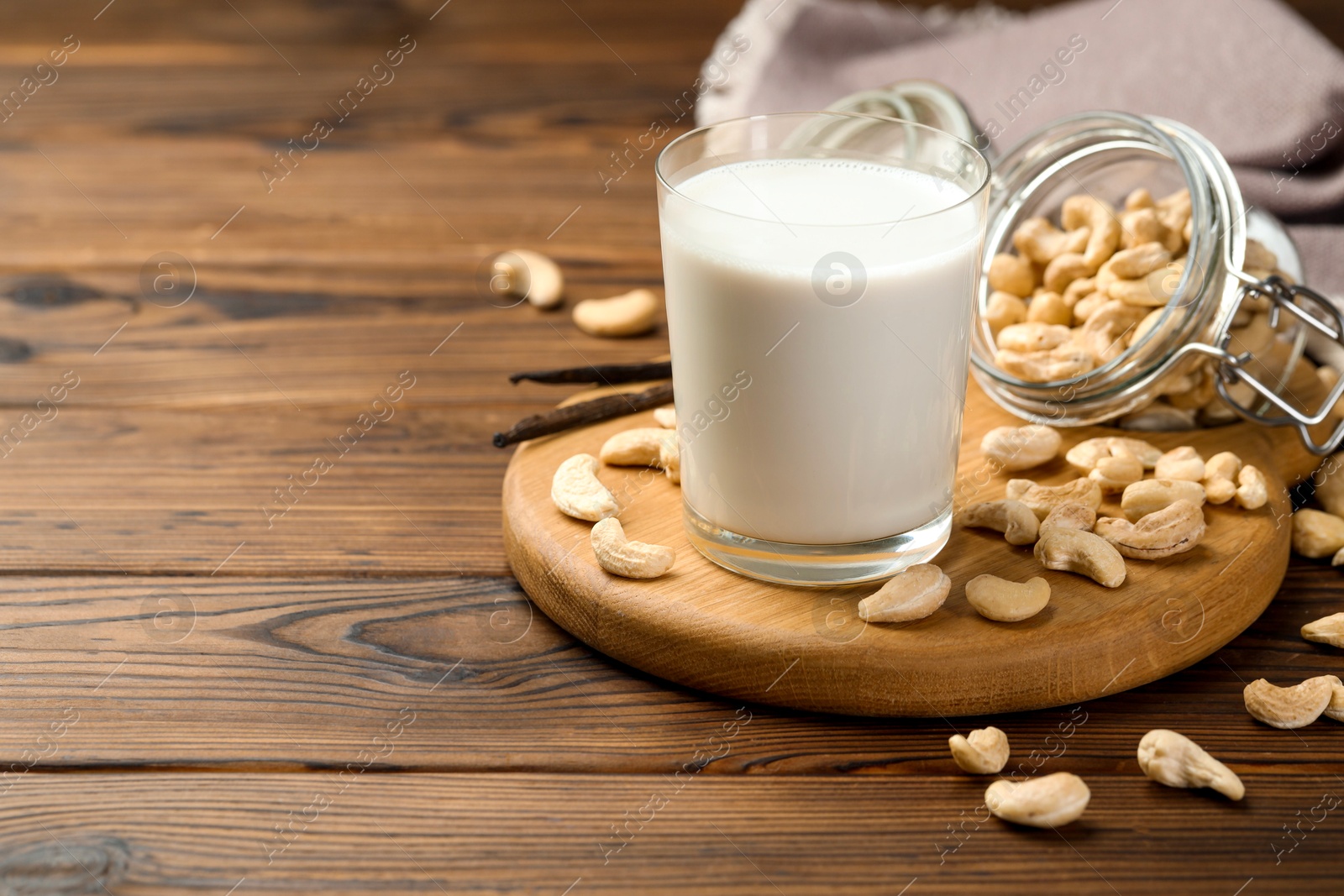 Photo of Fresh cashew milk in glass, nuts and vanilla pods on wooden table, space for text