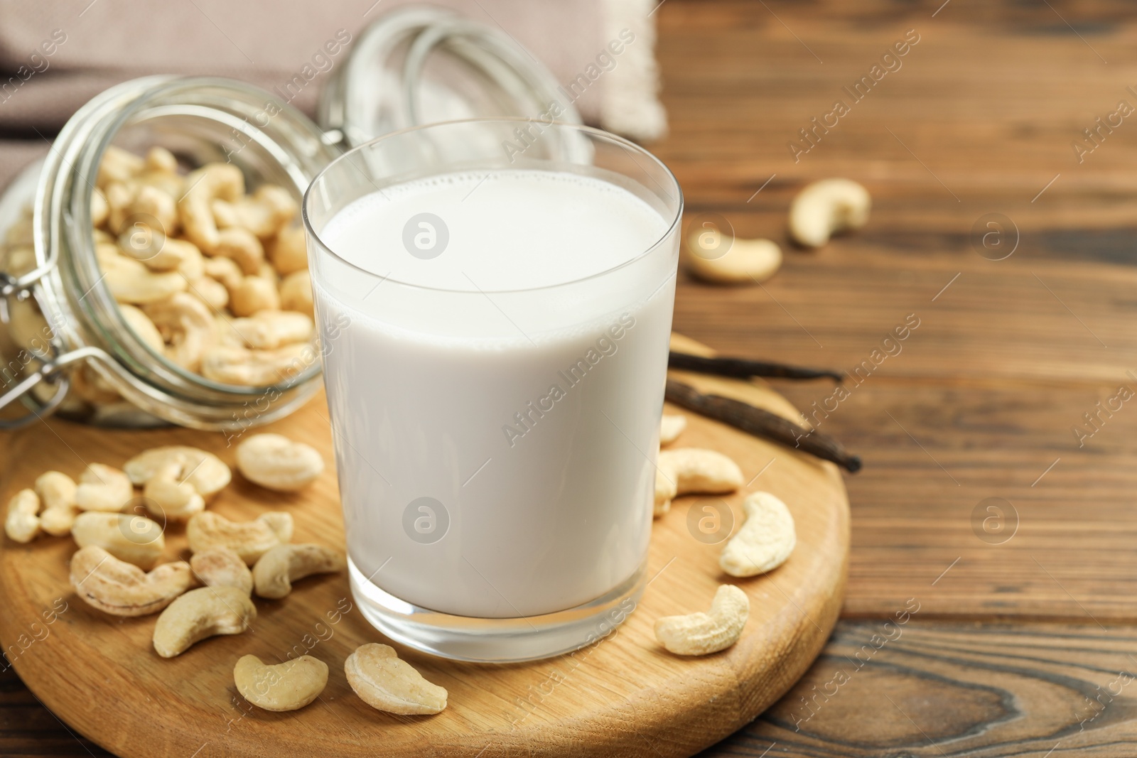 Photo of Fresh cashew milk in glass, nuts and vanilla pods on wooden table, closeup