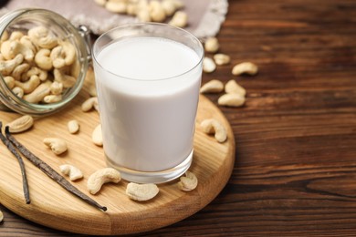 Photo of Fresh cashew milk in glass, nuts and vanilla pods on wooden table, closeup. Space for text