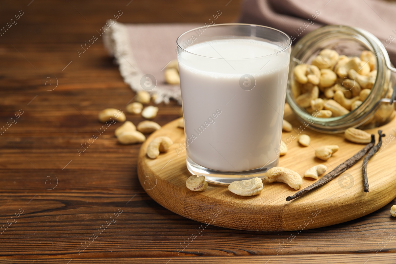 Photo of Fresh cashew milk in glass, nuts and vanilla pods on wooden table, closeup. Space for text