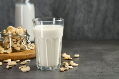 Fresh cashew milk in glass and nuts on grey table, space for text