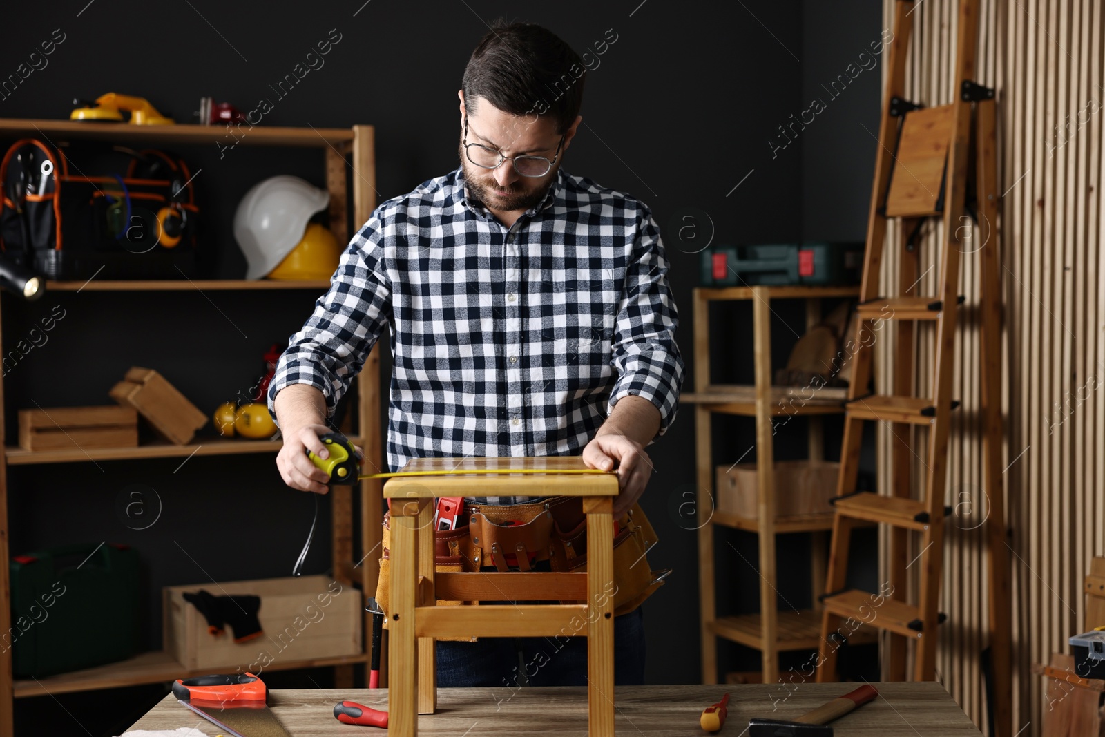 Photo of Repairman measuring wooden stool at table in workshop