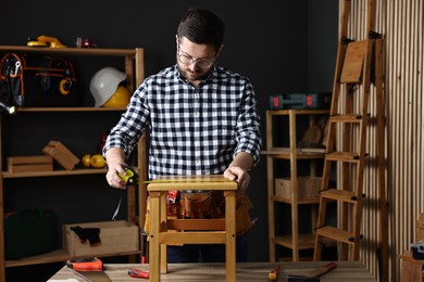 Photo of Repairman measuring wooden stool at table in workshop