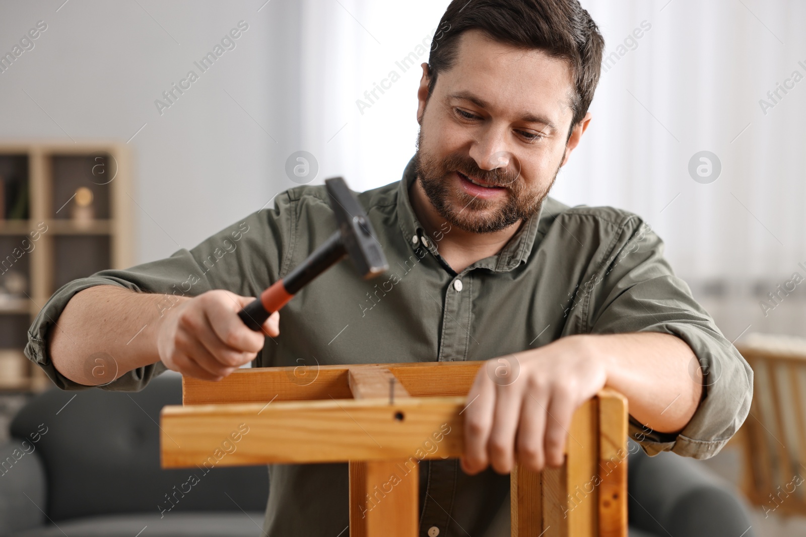 Photo of Man repairing wooden stool with nail and hammer at home