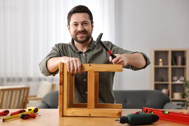 Photo of Man repairing wooden stool with nail and hammer at home